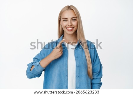 Happy smiling blond girl pointing finger at her teeth smile, showing dental clinic procedure result, standing over white background