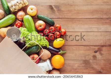 Paper grocery bag with fresh vegetables, fruits, milk and canned goods on wooden backdrop. Food delivery, shopping, donation concept. Healthy food background. Flat lay, copy space. Royalty-Free Stock Photo #2065641863