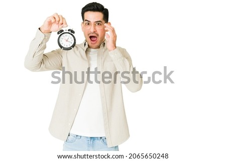 Surprised young man is late for an appointment and looking at the clock because the alarm didn't work