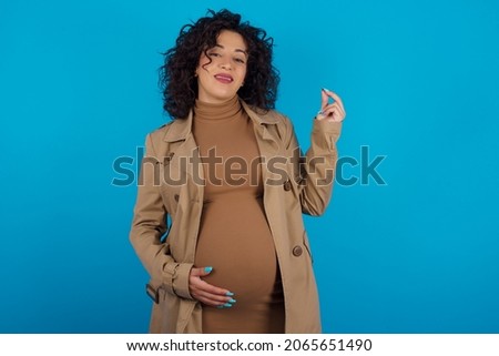 Young pregnant arab woman standing on blue studio background  pointing up with hand showing up seven fingers gesture in Chinese sign language QÄ«.