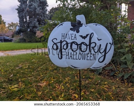 Lawn sign shaped as pumpkin have a spooky Halloween on a residential street in front of a house.