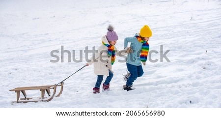 Happy kids having fun and riding the sledge in the winter snowy forest. Winter Christmas holidays and active winter weekend, children activities. Snow background, banner copy space.