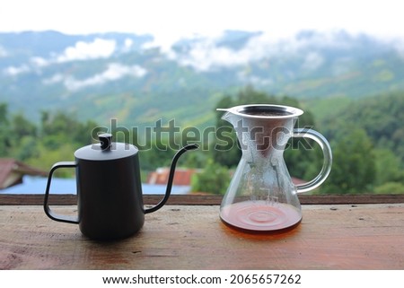 Glass cup with drip coffee  from kettle on wooden table in the nature background ,coffee time in the morning time with mountain view and natural green view feeling chill and relax.