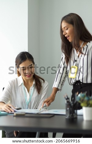 Female asian mentor teaching female trainee intern looking at report papers, female colleagues working together in office. Royalty-Free Stock Photo #2065669916