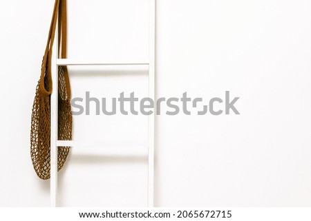 White staircase with a brown string bag on the background of a white wall. Creative background.