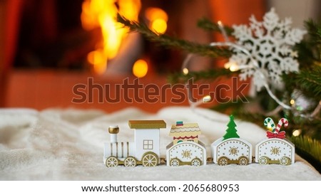 Christmas white, toy train, on the background of a Christmas tree and a lit fireplace. Garland bokeh, selective focus, space for text. Christmas card.