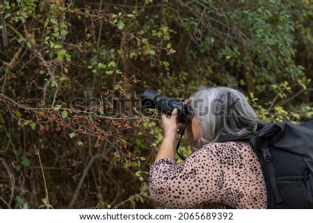 older white-haired woman taking pictures in the forest