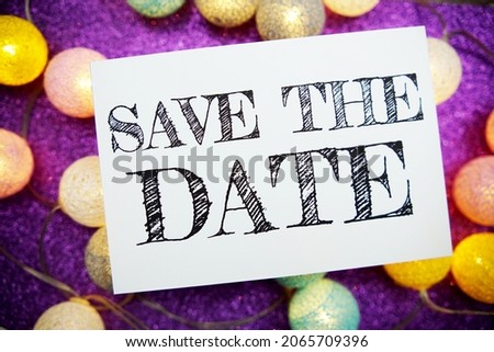 Save The Date text on paper card top view on purple bokeh background