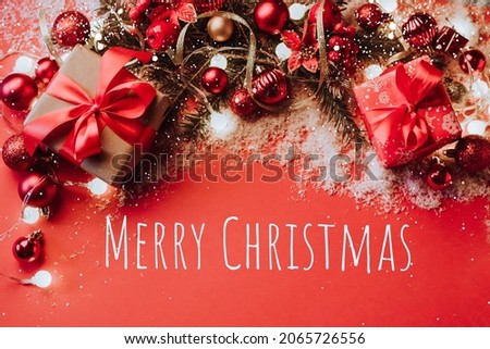 Christmas gifts red and gold Christmas balls garland fluffy fir branches red background with snowflakes, sparkles, confetti. Festive Christmas card template with phrase Merry Christmas