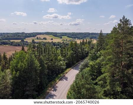 Areal drone photography of highway near forest and agrivculture fields. Photo taken on a warm overcast summer day.