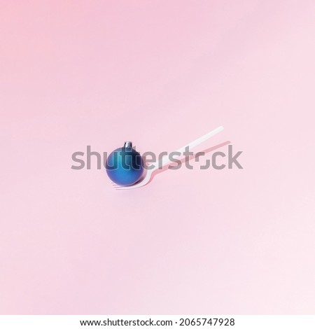 A Christmas and New Year blue bauble  stands on a white plastic fork on a pink background. Minimal design. Copy space.