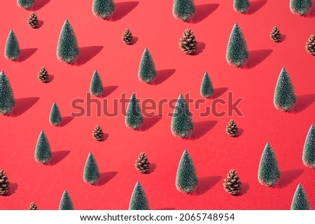 Arranged small and big green New Year and Christmas tree with brown pinecone on a red pastel background. Pattern.