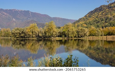 Italian mountain autumn landscape. Revine lake in yellow green colors. Reflection of trees and mountains in the lake. Relaxation concept.