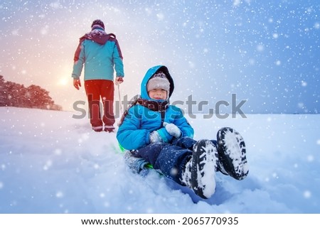 Father pulling sled with his lovely smiling son in snowfall. Concept of the family relationship and vacation.