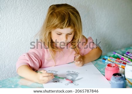 Little creative toddler girl painting with finger colors koala bear. Active child having fun with drawing animals at home, in kindergaten or preschool. Education and distance learning for children.