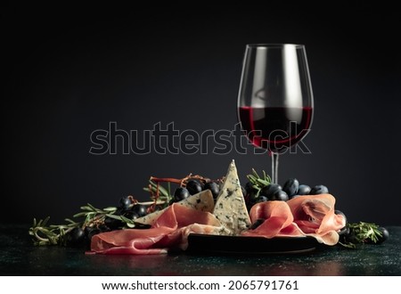 Red wine with grapes, rosemary, prosciutto, and blue cheese on a dark background. 