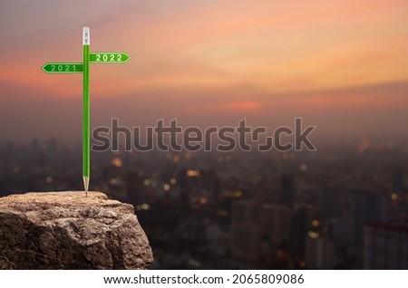 2022 and 2021 direction sign plate with green pencil on rock mountain over cityscape on warm light sundown, Business strategy planning concept, Happy new year 2022 calendar cover