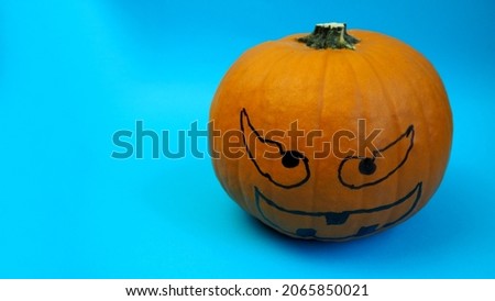 halloween. a pumpkin with a marker drawn on its face, for a holiday, stands on a blue background. side view