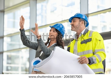 Woman architect explaining blueprint to supervisor at construction site. Mid adult contractor holding blueprint and understanding manager vision at construction site. Engineer talking to contractor.