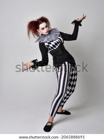 Full length  portrait of red haired  girl wearing a black and white clown jester costume, theatrical circus character.  Standing pose  isolated on  studio background.