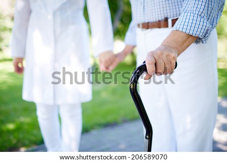 Close-up of disabled female hand holding cane with her doctor walking near by