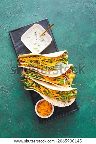 Plate with tasty tacos and sauce on color background