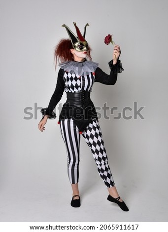 Full length  portrait of red haired  girl wearing a black and white clown jester costume, theatrical circus character.  Standing pose  isolated on  studio background.