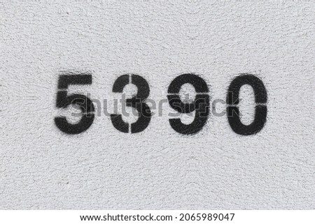 Black Number 5390 on the white wall. Spray paint. Number five thousand three hundred ninety.