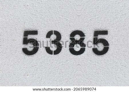 Black Number 5385 on the white wall. Spray paint. Number five thousand three hundred and eighty five.