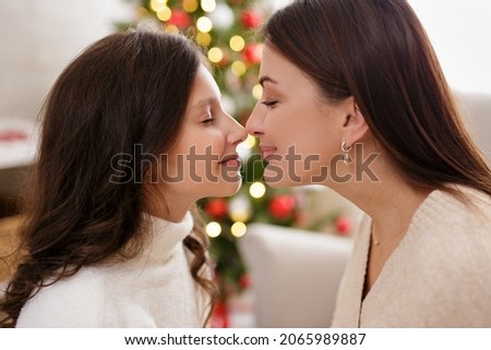 Christmas, family, love and motherhood concept - close up portrait of happy mother and her cute daughter in decorated living room with Christmas tree