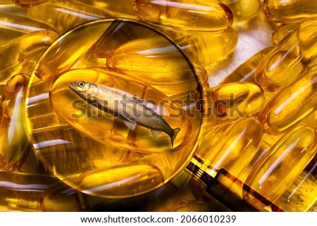 Magnifying glass zooms in on the omega3 capsule with a live fish inside. Concept of how to choose omega3. Choosing the best natural fish oil.  Royalty-Free Stock Photo #2066010239