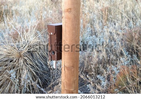 Brown outdoor trail camera on wooden post. Monitor hiking and trail activity.                               