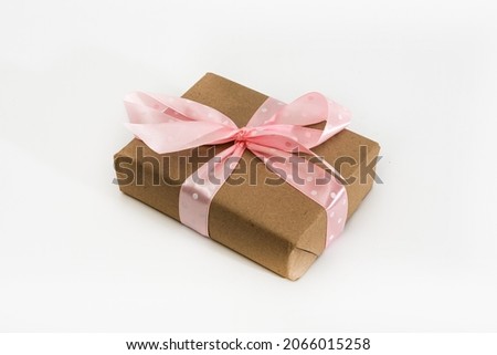 Gift wrapped in brown paper and tied with a pink ribbon on a white background. Isolated.