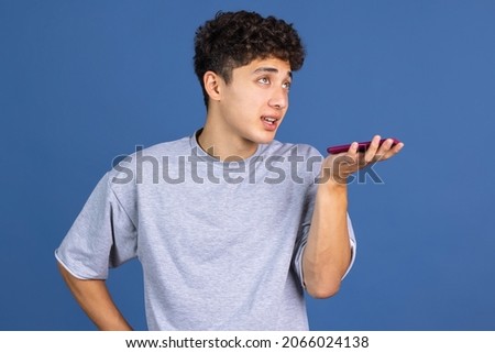Chatting. Portrait of young curly man, student using phone isolated over blue studio background with copyspace for ad. Concept of human emotions, facial expression, youth culture, diversity