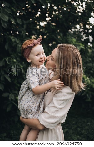 Young mother hugging her little daughter. Mom kisses and hugs her child on nature. Concept of family, motherhood, child. A walk with kid in nature. Love and relationship.