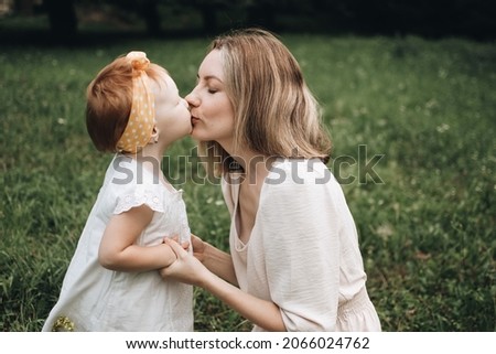 Young mother hugging her little daughter. Mom kisses and hugs her child on nature. Concept of family, motherhood, child. A walk with kid in nature. Love and relationship.