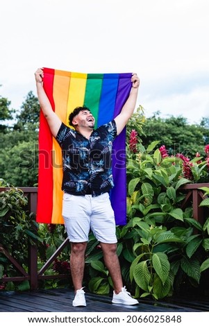 Young gay man with diversity flag outdoors very happy