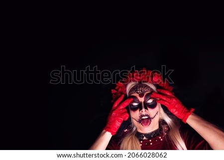 Closeup portrait of scary young woman dressed as a witch for Halloween, showing tongue, with her whites of eyes visible; isolated on black background
