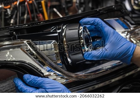 A mechanic wearing rubber gloves installs an LED lens into the headlight housing.Car headlight during repair and cleaning.The mechanic restores the headlight of the car.Restoration of automotive optic Royalty-Free Stock Photo #2066032262