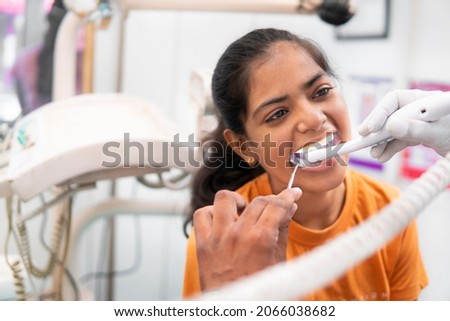 Indian female, young patient sitting on chair with open mouth and dentist examining her teeth with the intraoral camera at the clinic.   Royalty-Free Stock Photo #2066038682