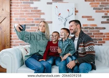 Young family having fun talking on a video call using a mobile phone, rejoicing and smiling, husband wife and your guys brothers greet friends with New Year and Christmas holidays