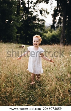 Little girl is running on meadow. Child playing in the park and a dog is on a background. Childhood.