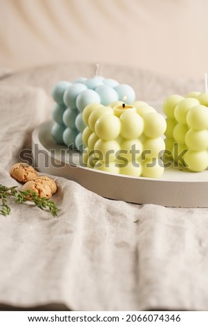 Green, blue and white square bubble candles on a concrete tray on a linen table cloth