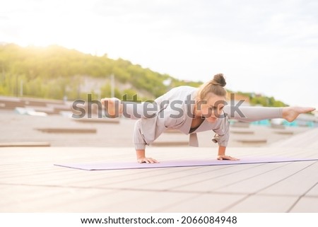 Low-angle view of flexible young yogini woman practicing yoga exercisers on fitness mat on summer day outdoors in city park. Calm female with beautiful body in sportswear performing asana pose outside