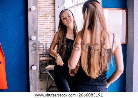 A young woman looks at her reflection in the mirror. The girl is in a good mood, smiling. Fashionable modern look.