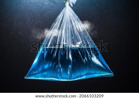Plastic bag with water and a paper boat inside over a black background. Not knowing what direction to take or without realizing what is beyond the small space we live in. Concept photo. Royalty-Free Stock Photo #2066103209