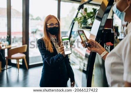 Young attractive business woman showing digital Covid-19 immunization pass certificate to the security guard on a restaurant or cafe bar entrance. Pandemic and global security measures concept. Royalty-Free Stock Photo #2066127422