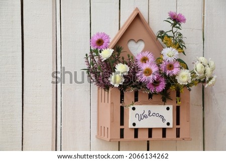 White wooden garden fence with welcome sign on a wooden flower box. Bouquet of autumn flowers (aster, heather and chrysanthemum)