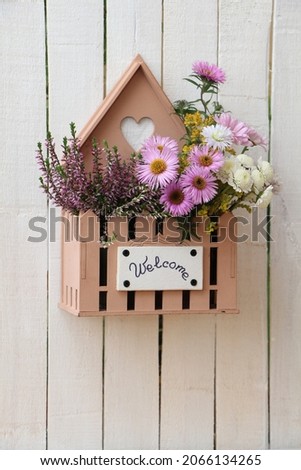White wooden garden fence with welcome sign on a wooden flower box. Bouquet of autumn flowers (aster, heather and chrysanthemum)
