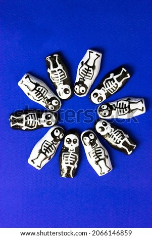 Trick or treat chocolate candies in the shape of black and white skeletons on blue background with round frame for text inside it. Halloween sweets and treats. October 31st. Funny scary characters